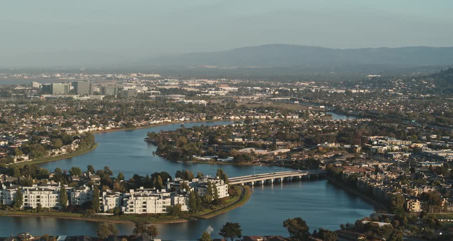 Fog obscures mountain on horizon backing city as traffic crosses bridge over winding river
