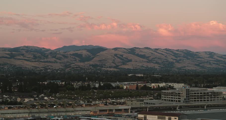 City buildings and streets with mountains in the distance under a cloudy pink sky