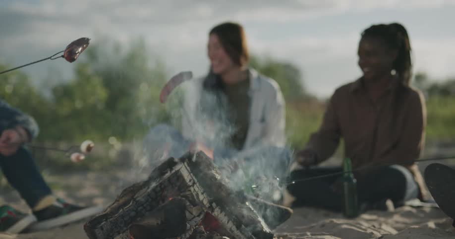A group of people cooking hot dogs over a camp fire