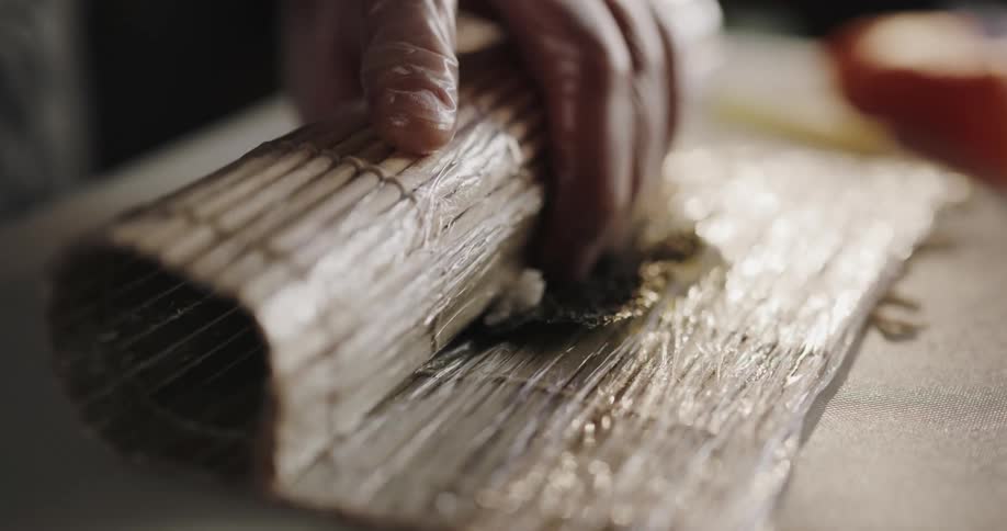 A person puts seafood on a sushi roll and then rolls it up