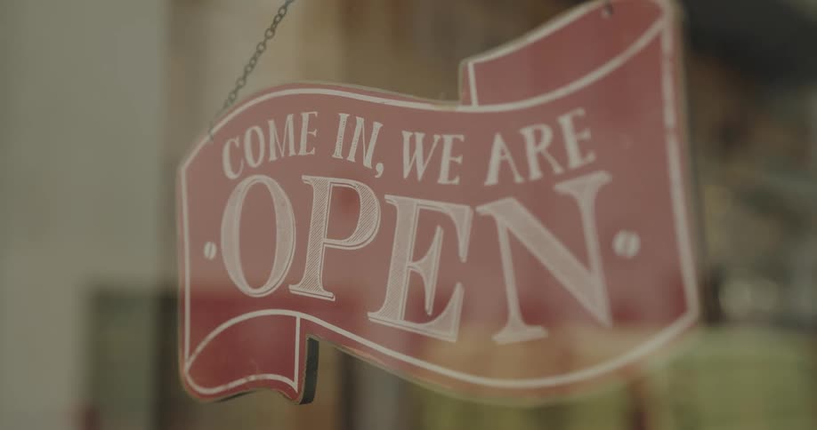 Hands flip a store sign in the window from closed to open