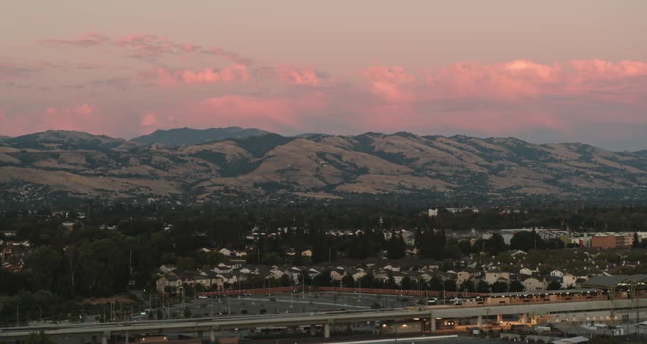 A city with roads buildings and trees with a mountain range the sky and clouds in the background