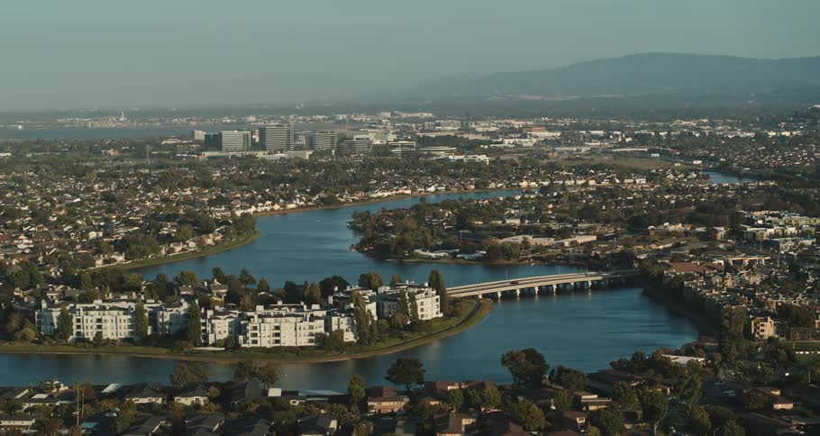 A city with a river and a bridge with buildings trees the sky and clouds in the background