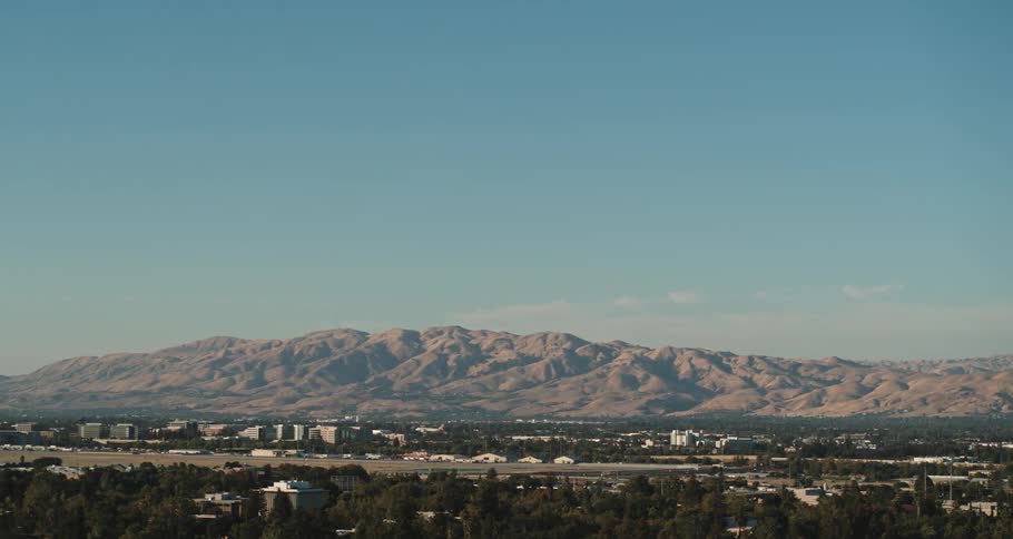 An airplane landing on a runway with a mountain range the sky and clouds in the background