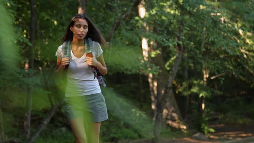 A woman in a white shirt walks down a forest path