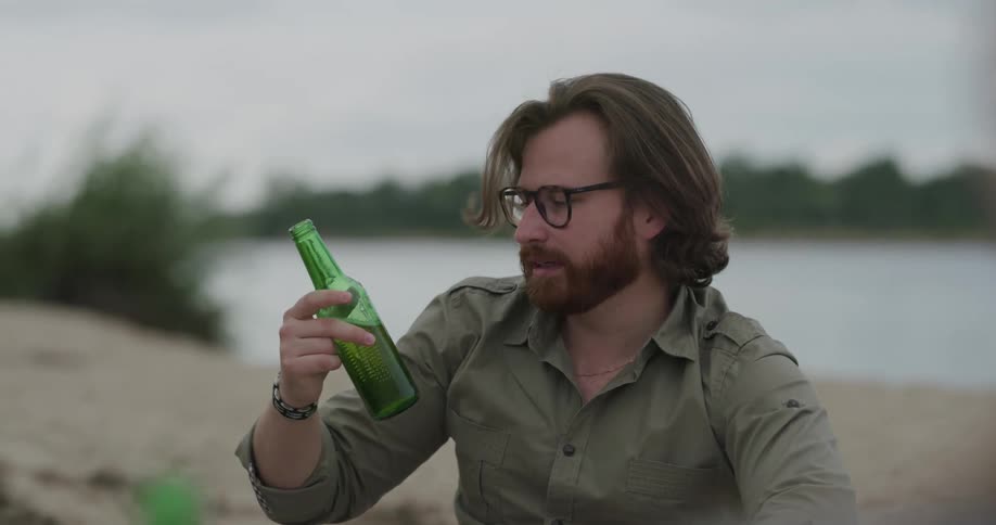 A man and a woman sitting and drinking beer with grass a river the sky and clouds in the background