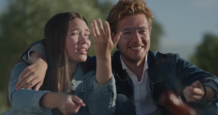 A couple is sitting around a campfire roasting food and laughing