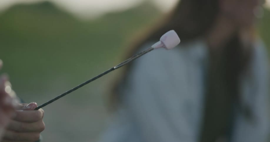 A couple laughs and talks while the man puts marshmallows on a stick