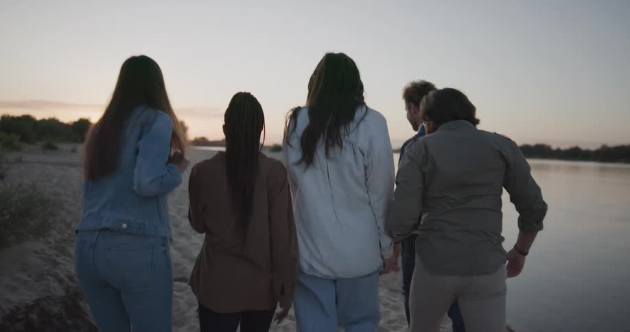 A group of friends laugh and walk with their arms around each other on the beach
