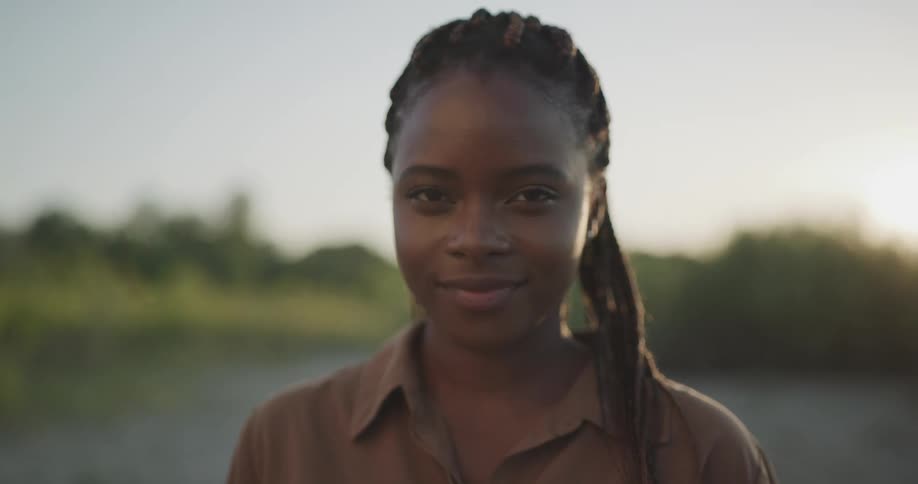 A young woman smiles into the camera while standing in the soil outdoors during the day