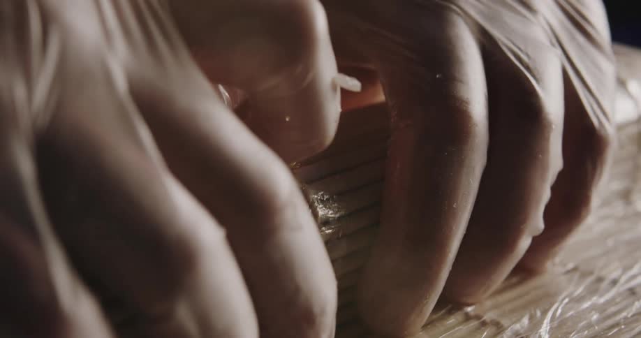 A person wearing latex gloves preparing sushi using a bamboo mat over a table