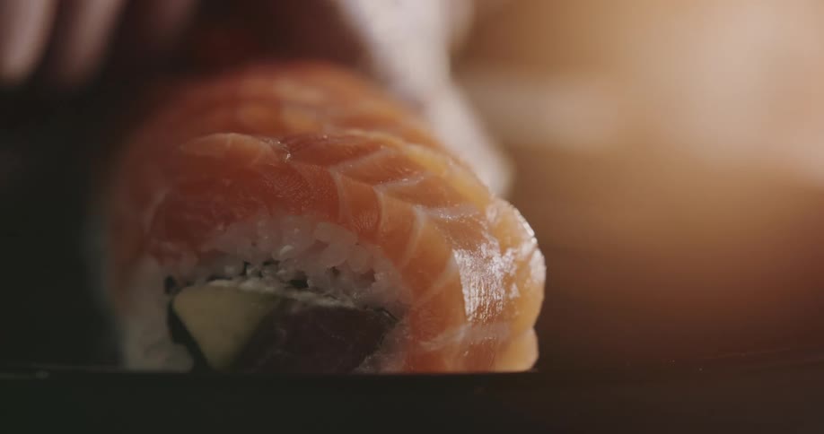 Person wearing gloves plates fish sushi rolls
