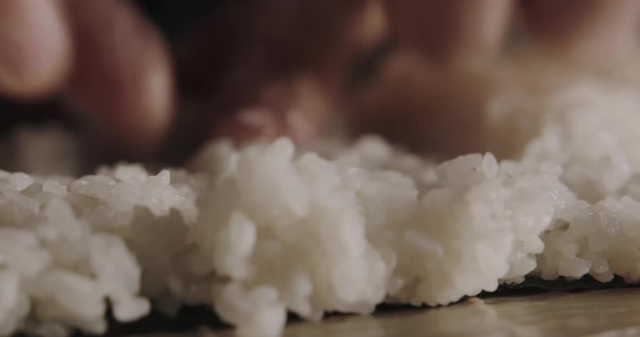 A person with gloves placing rice on seaweed on a table