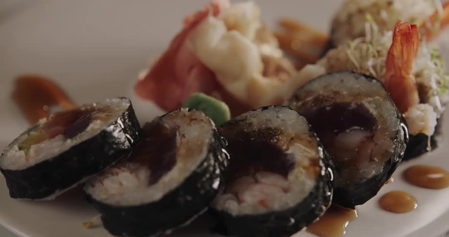 Sushi on a plate with sauce being drizzled on it and with seeds being sprinkled on it