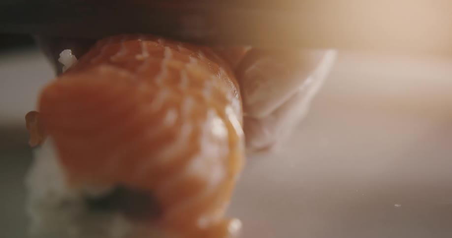 A cook wearing plastic gloves uses a knife to a sushi roll