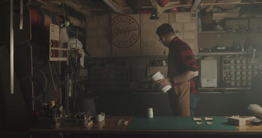 A man with glasses and an apron in a workshop with a wall in the background