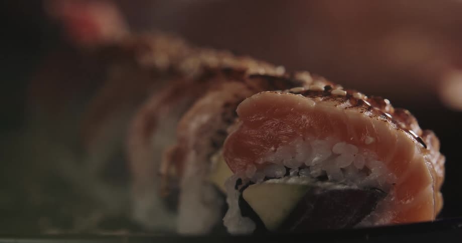 A person sprinkles sesame seeds on a sushi roll