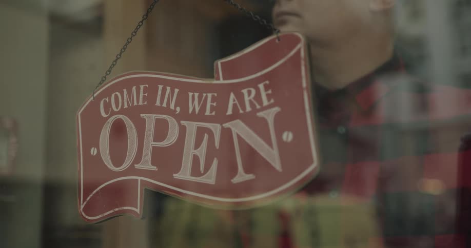 Man looks out through glass at opposite building before turning sign to closed