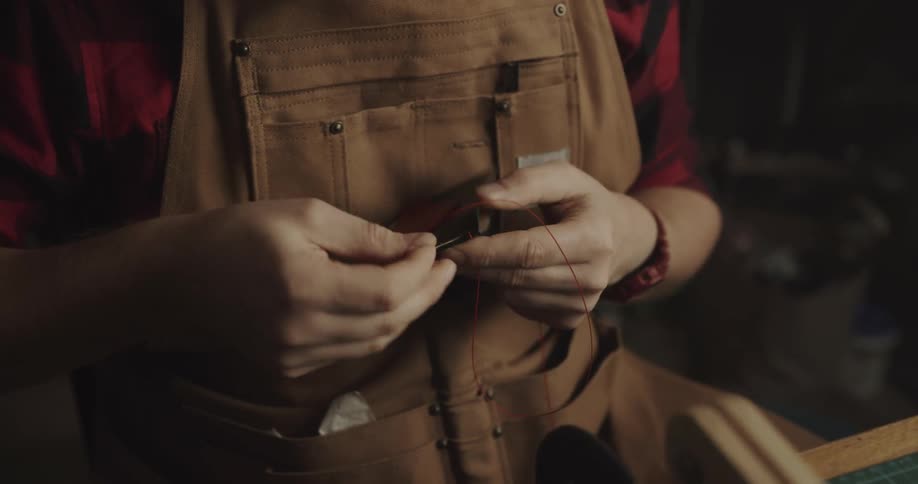 A man is threading a wallet with a needle