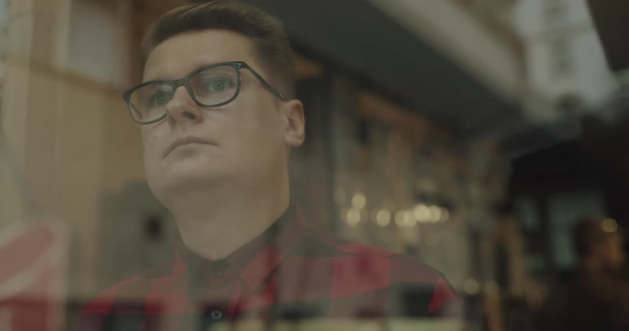 A man approaches the window of a business and gazes out for a moment before flipping business sign from open to closed