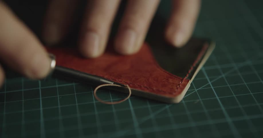 A person uses a tool to shave a strip of leather
