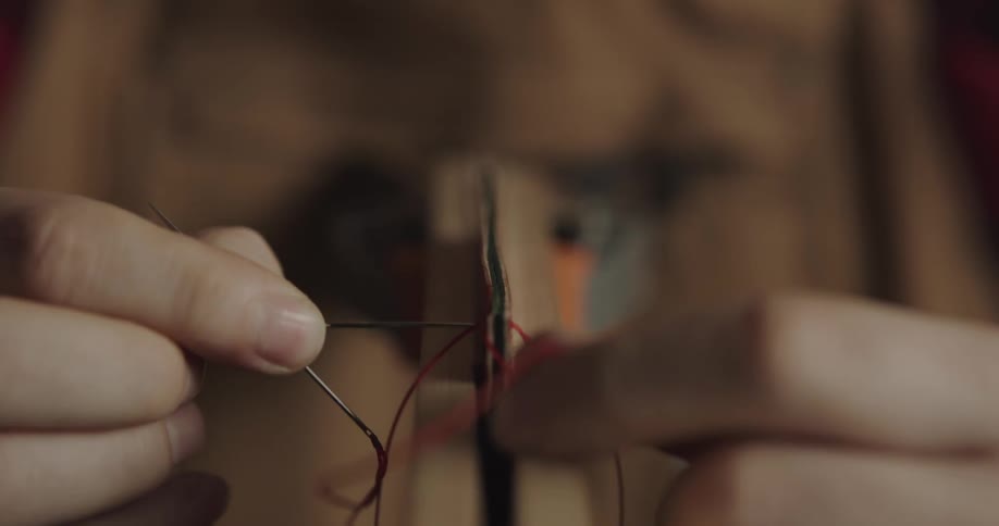 A craftsman uses two needles to sew leather together