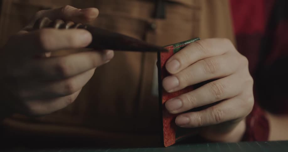A man uses a tool and rubs a piece of leather as he crafts