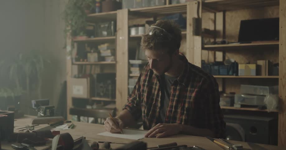 A man in a workshop drawing on a paper with a pencil