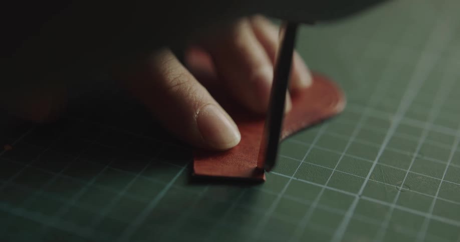 A leatherworker uses a tool to detail a piece of leather