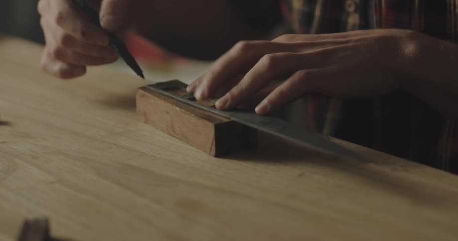 A person in a workshop marking out a handle for a knife with wood and a pen
