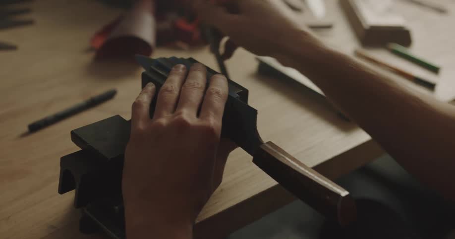 A man puts a large knife in a manual knife sharpener and turns the handle