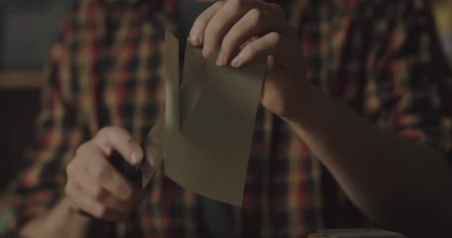 A man holds a piece of paper in his hand and slides a knife down it and cuts it