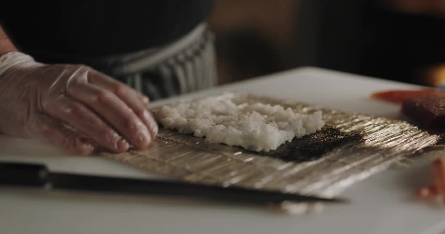 A man spreads sushi rice on seaweed as he prepares a sushi roll