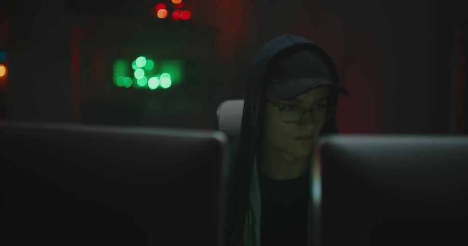 A teenage boy puts a chip in his mouth as he sits in front of two computer screens