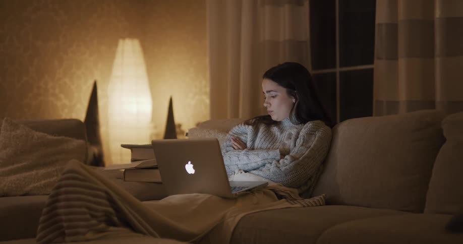 White teenager girl video calling someone on her laptop while sitting at the couch