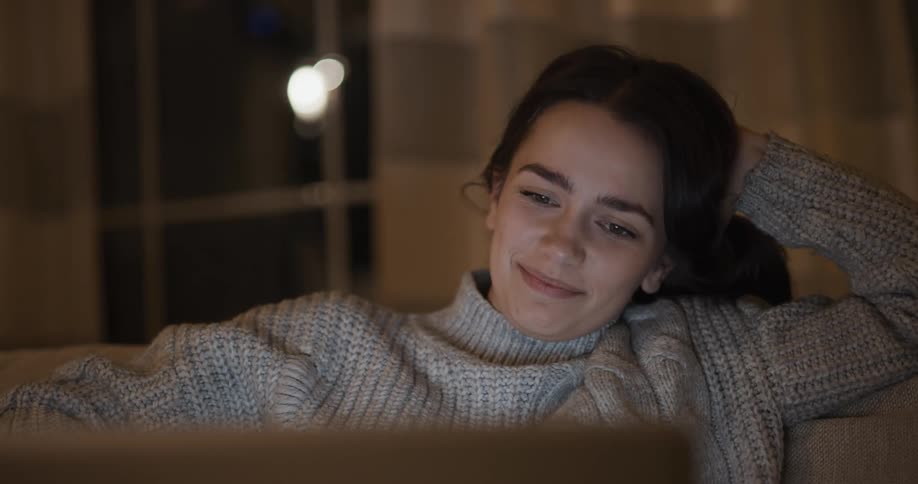 A teenage girl sits at home and talks with someone on a computer