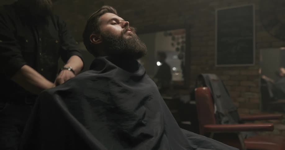 A barber wraps an apron around a customer sitting in his styling chair