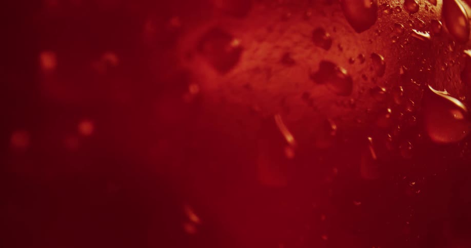 Droplets of water over the surface of a glass filled with a bright red liquid