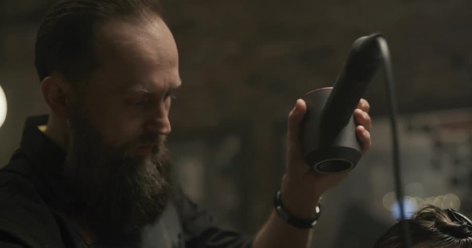 A hair stylist combs a mans hair with one hand while using a hair dryer with the other