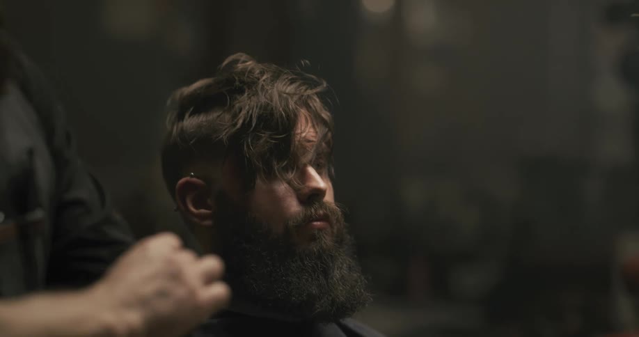 A barber removes the clip from the top of his clients hair and spritzes it