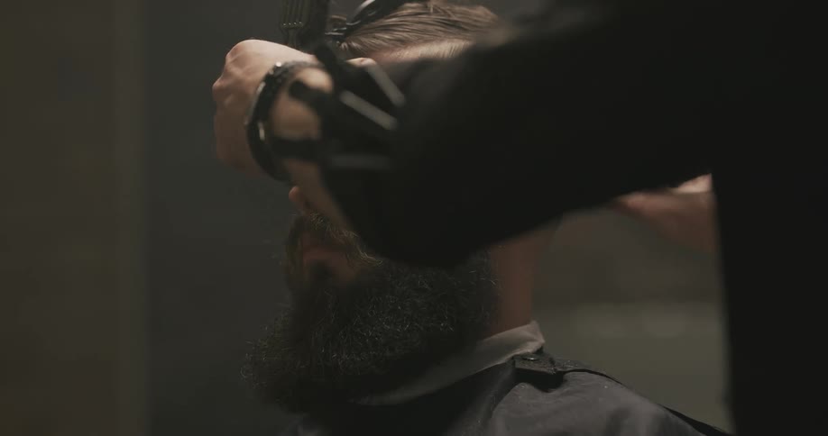 A man in a barbershop cutting another mans hair with electric clippers