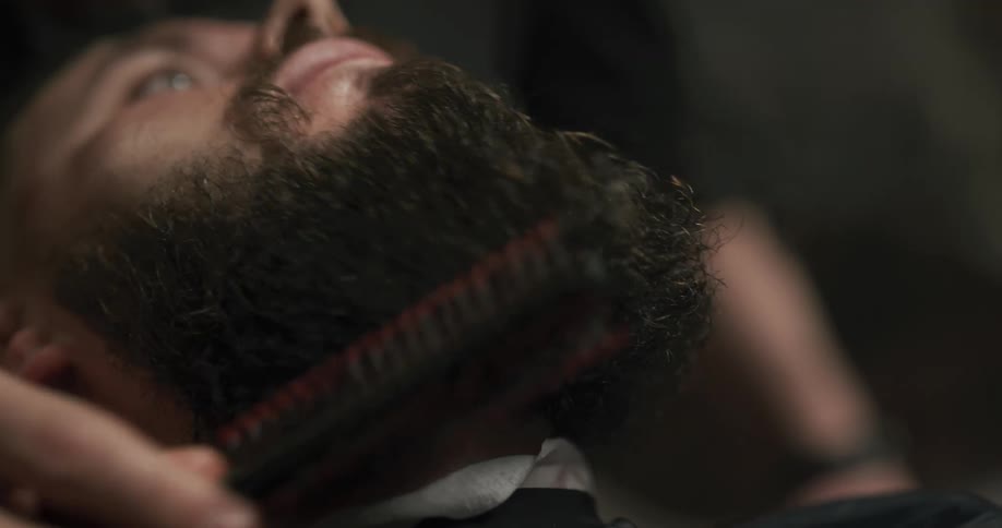 A man sitting in a barbershop getting his beard combed