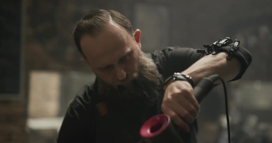 A barber with a full beard dries and combs the beard of a client
