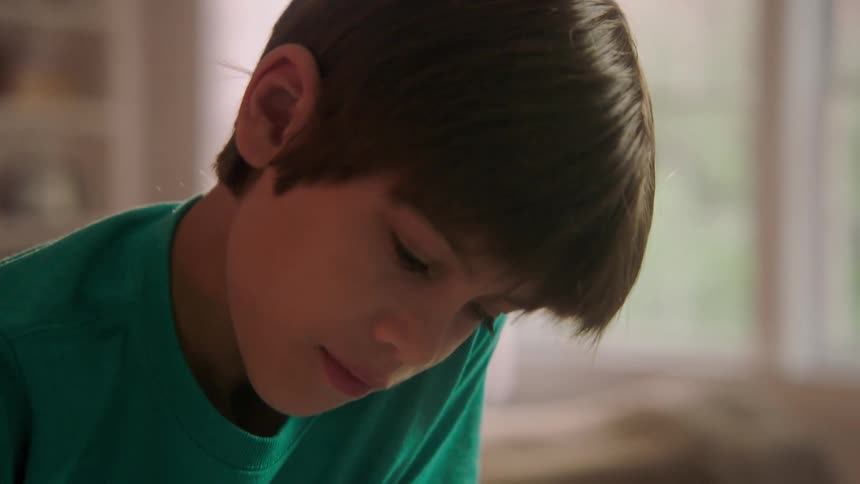 A boy is writing in his home with a pencil