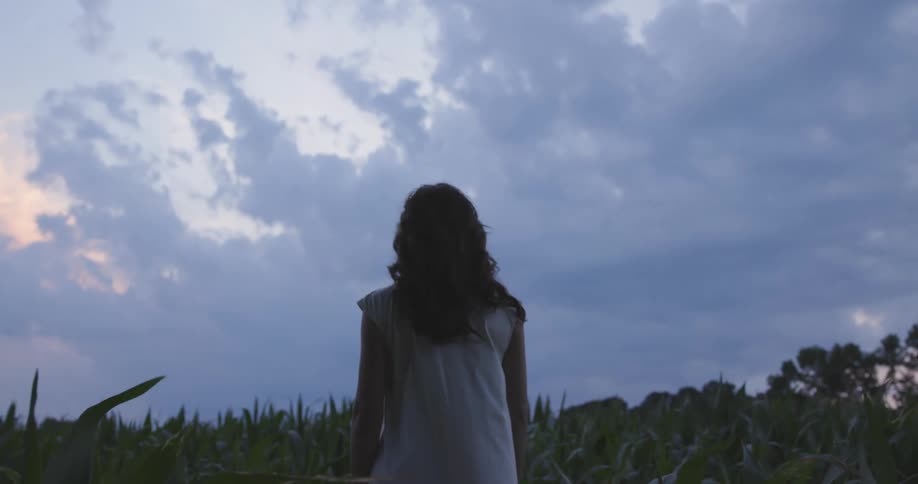 White woman wearing a white evening dress stading in the middle of a tall grass