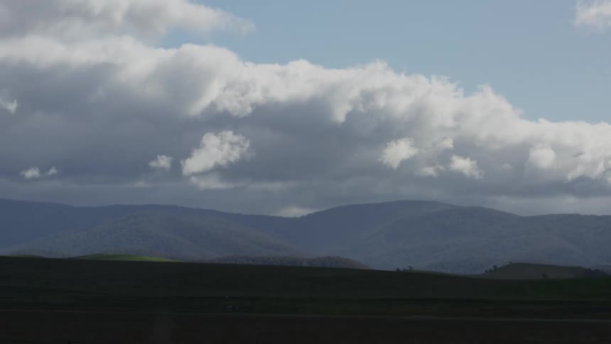 Clouds moving across the sky over mountains and grass below