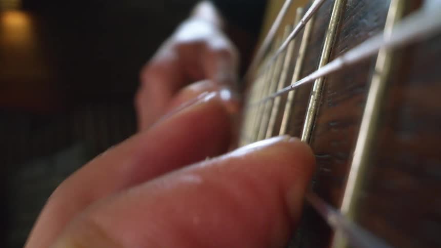 Person is playing a guitar and moving their fingers and strings along the frets