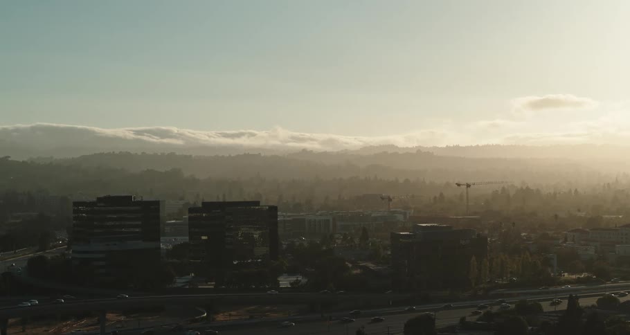 Busy city with many cars on the streets and buildings in town with mountains and clouds on the horizon with a bright sun