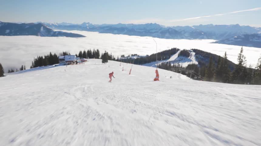Snowboarder in orange snowsuit rides down a snow covered hill with mountains on the horizon