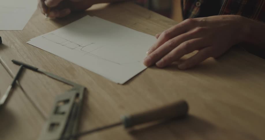 A man sketches with a pencil on a workbench covered with woodworking tools